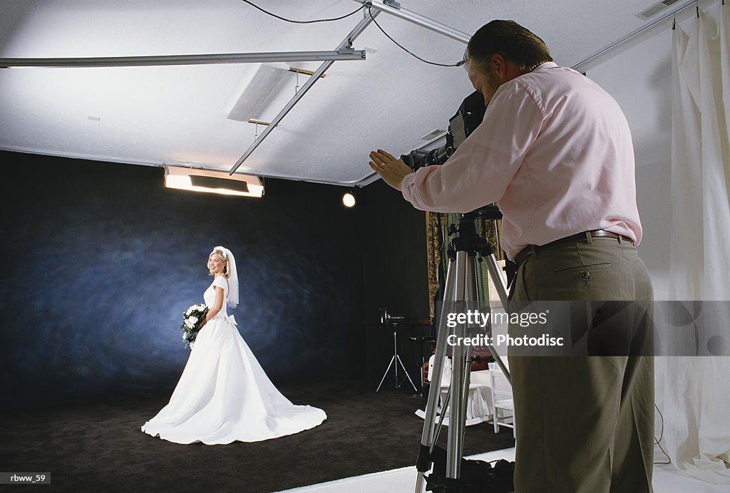 A caucasian bride poses in her bridal gown for a photographer in his studio
