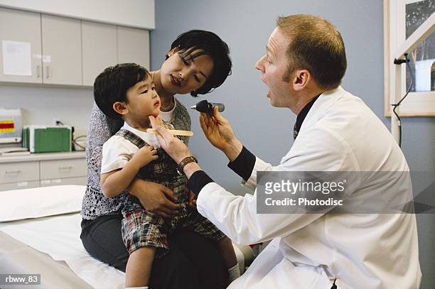 a caucasian male physician conducts a routine check-up on an asian boy with his mother - check up ストックフォトと画像