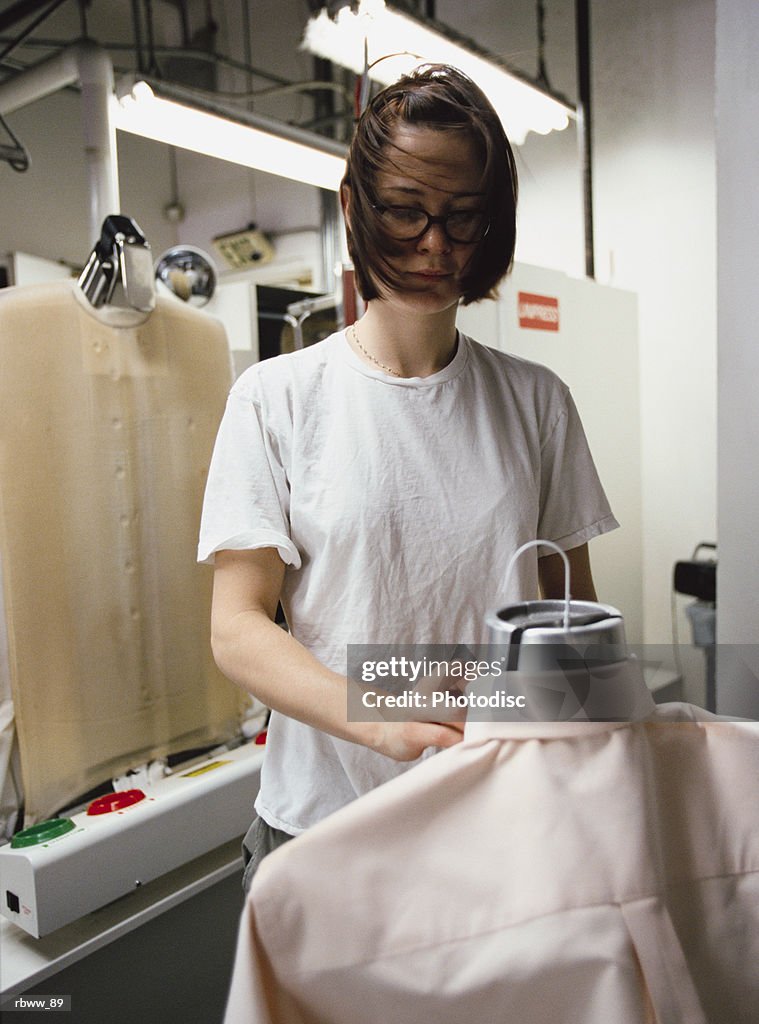 A brunette caucasian female prepares a shirt to be pressed at the cleaners