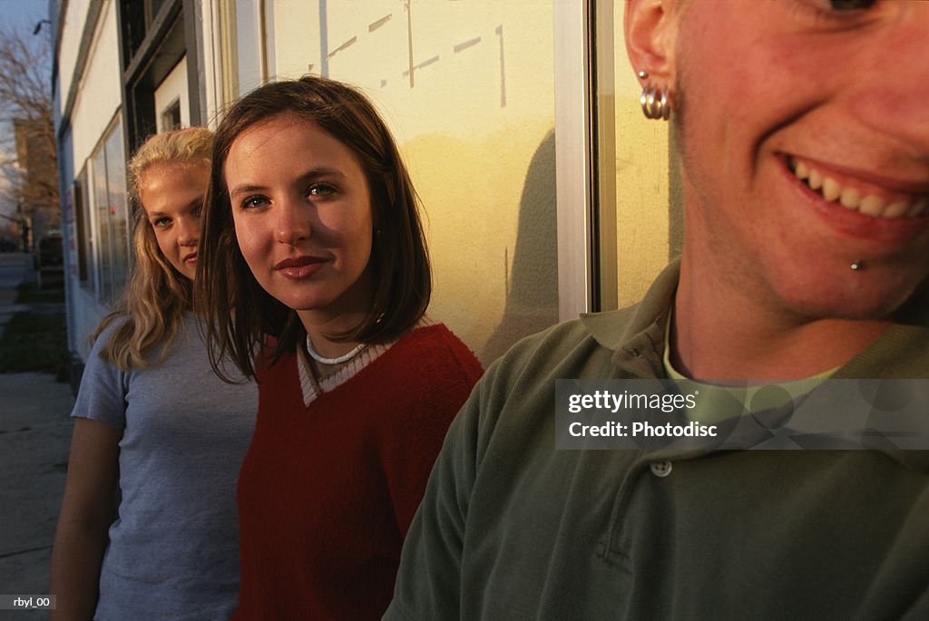 Three teenagers on the sidewalk of a city block looking into the camera