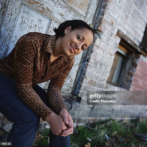 young woman in orange long sleeve shirt blue jeans sits on the doorstep of old abandoned building - long - fotografias e filmes do acervo