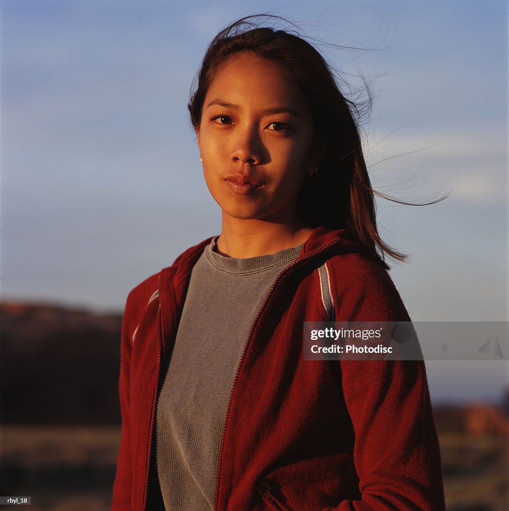 A young woman in a grey shirt and red jacket is standing in the south utah desert with the desert blurred in the background