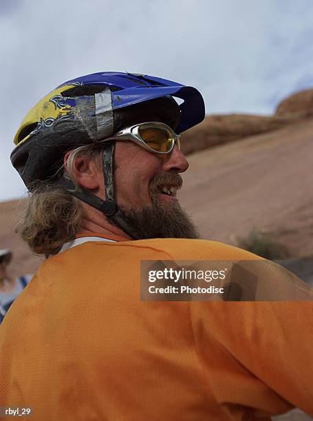a man with a long beard and bicycle helmet is smiling happily with the southern utah desert and sky in the background - long - fotografias e filmes do acervo