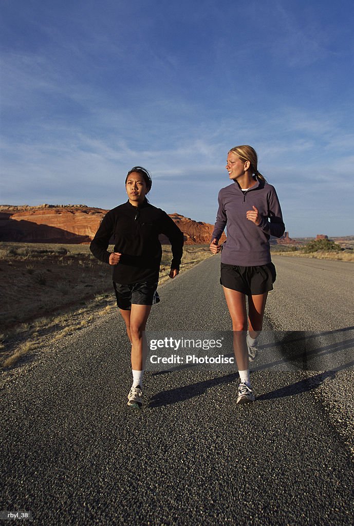 Two young women in shorts and long sleeve shirts are running along a road in the south utah desert