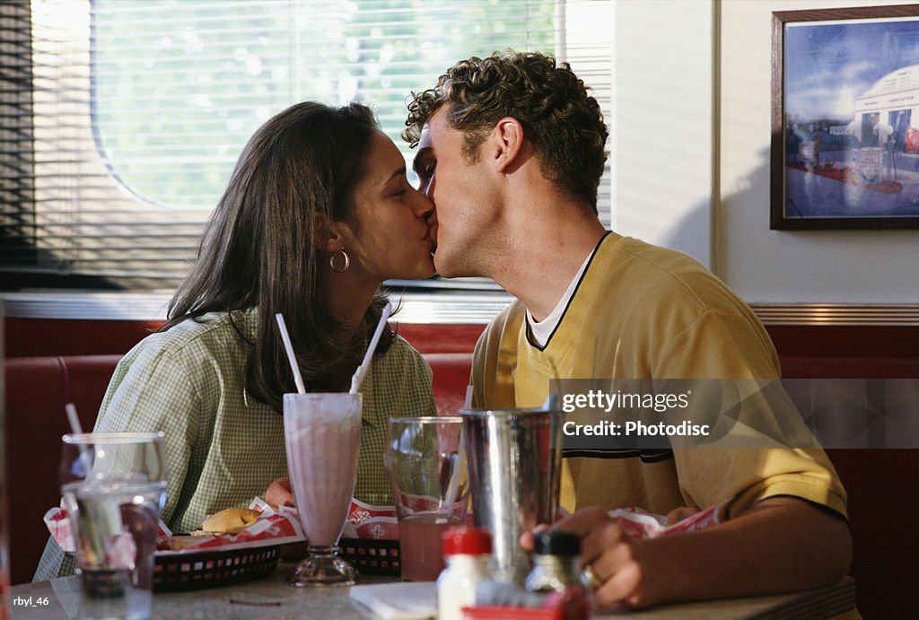 A young couple in a restaurant booth are kissing