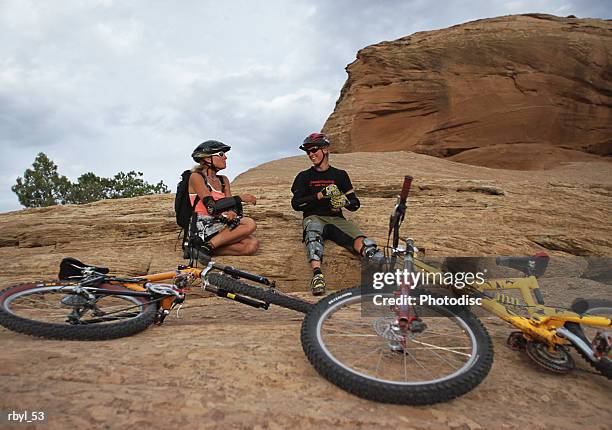 a man and a woman are resting on a rock in moab utah with thier mountain bikes laying down in front of them - valley type stock pictures, royalty-free photos & images