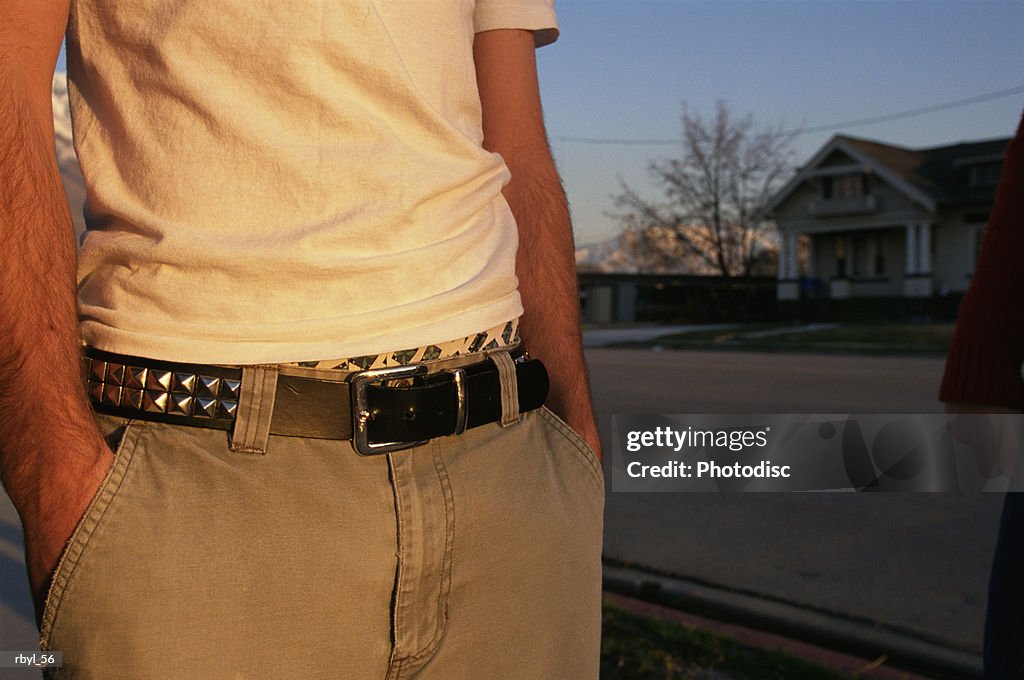 The mid-section of a teenage boy in a yellow shirt and tan pants with his hands in his pockets