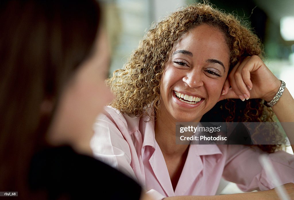 A young woman in a pink shirt is laughing and talking to a friend
