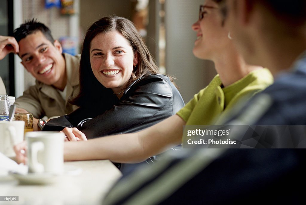 A group of young adults are sitting at the counter of a diner or cafe laughing and talking to eachother