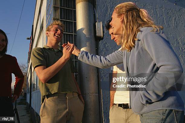 a spiked haired young man in green shirt and tan pants is greeting a young girl in a blue long sleeved sweatshirt and blue jeans on a street corner - blue corner stockfoto's en -beelden