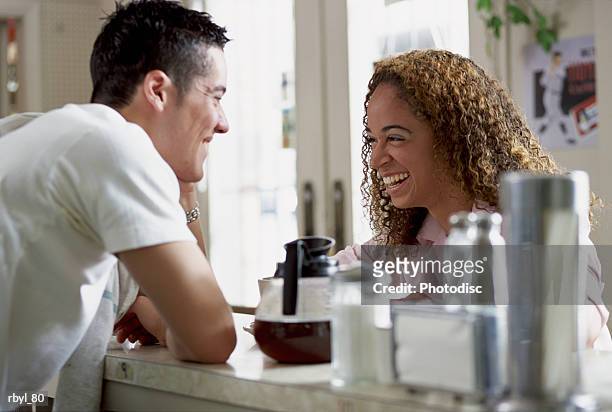 a young man working the counter of a restuarant or cafe is laughing and tlaking with a young woman with curly brown hair - curly stock pictures, royalty-free photos & images