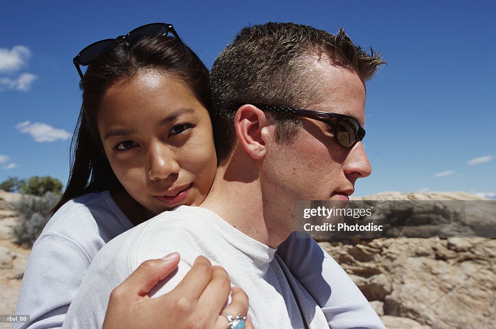 A head shot of a young couple standing in an embrace with the young lady looking at the camera and the young man standing profile to the camera with the south utah desert in the background