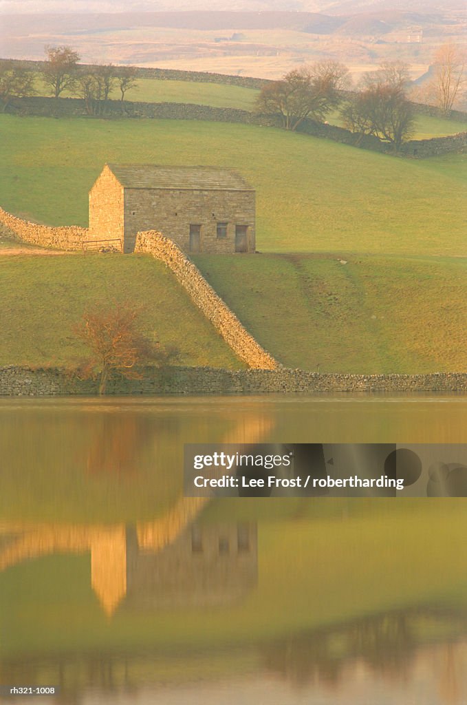 Barn and wall reflected in water at dusk, near Muker, Yorkshire Dales National Park, North Yorkshire, England, UK, Europe