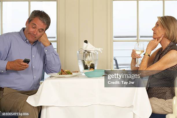 mature couple sitting at table in restaurant, man using mobile phone - ignore stock pictures, royalty-free photos & images