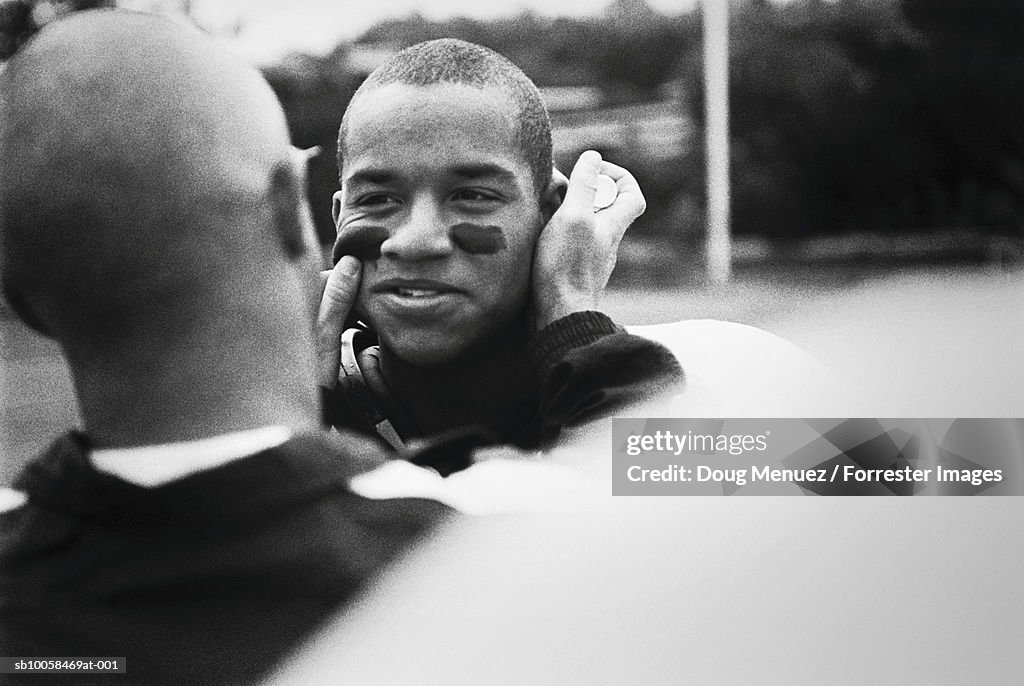 American footballer painting team-mates face, outdoors (B&W)