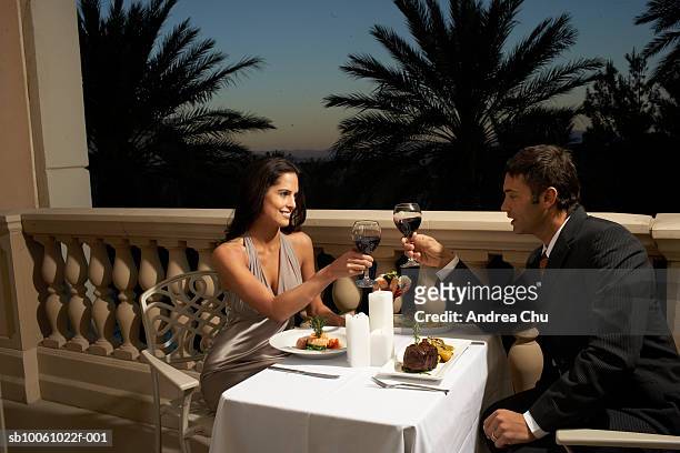 couple in evening wear having dinner on balcony, toasting with red wine - abbigliamento elegante foto e immagini stock