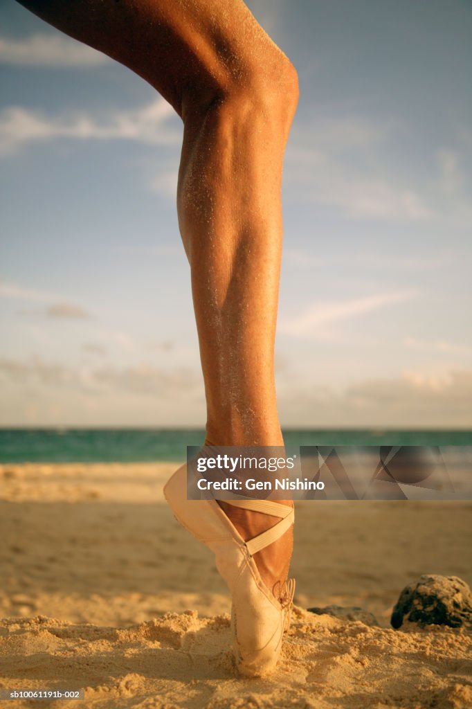 Woman wearing ballet shoe on beach, low section