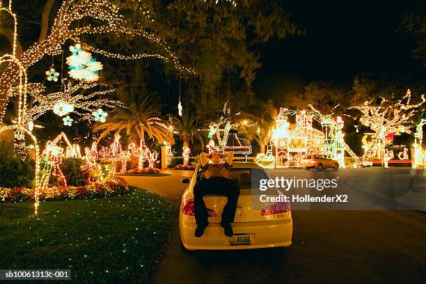 man lying on car at night with illuminated trees around - decorated christmas trees outside stockfoto's en -beelden