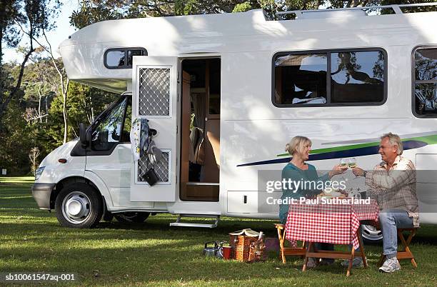 mature couple having picnic by motor home in park, toasting - camper van stockfoto's en -beelden