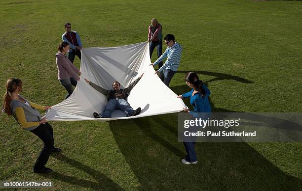 group of people in park holding large white sheet with man lying inside - safety net stock pictures, royalty-free photos & images