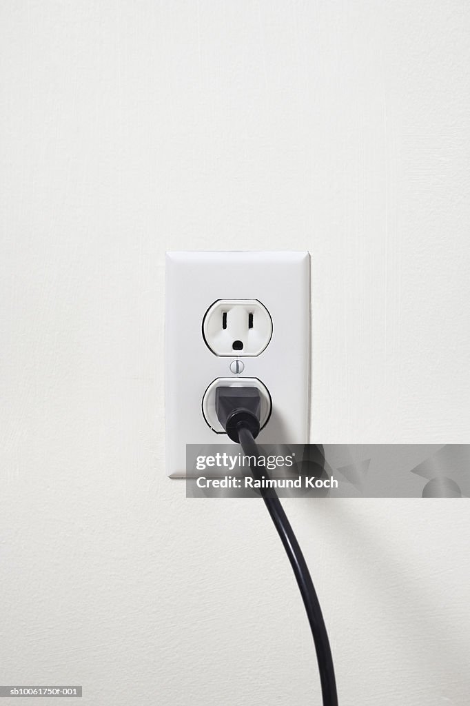 Electrical cord plugged into outlet on white wall