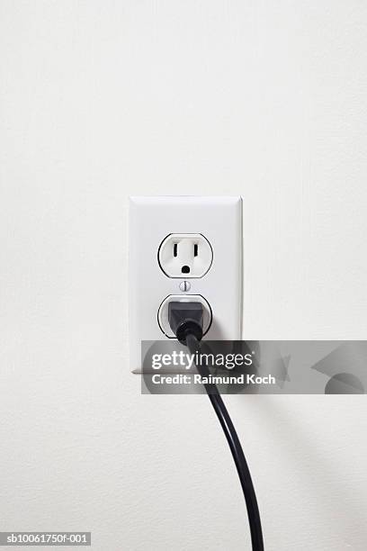 electrical cord plugged into outlet on white wall - power plug stockfoto's en -beelden
