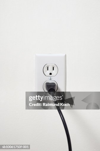 Electrical cord plugged into outlet on white wall Electrical cord plugged into outlet on white wall