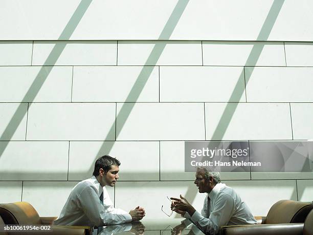two businessmen having discussion in hotel lobby, side view - two people talking face to face stock-fotos und bilder