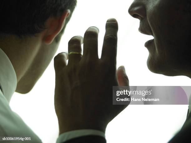 businessman whispering another businessman, close-up - rumor foto e immagini stock