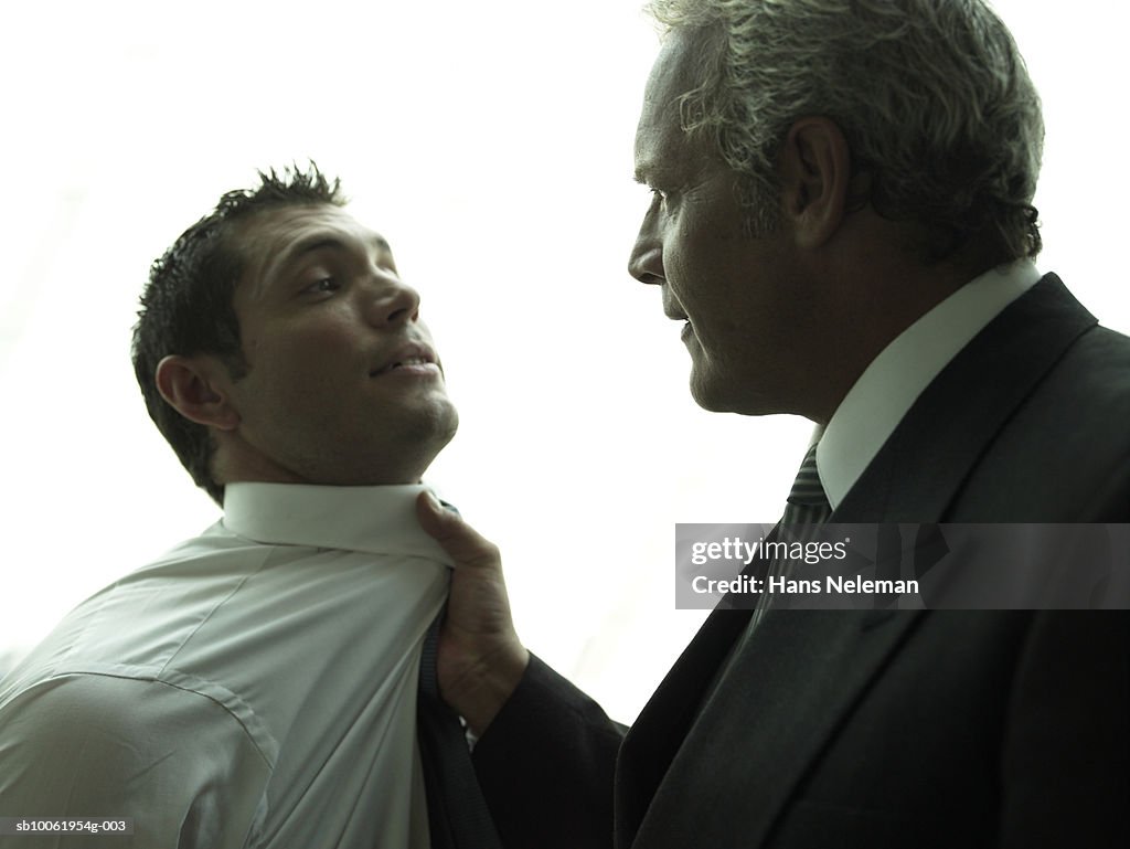 Mature businessman gripping young businessman's collar, close-up