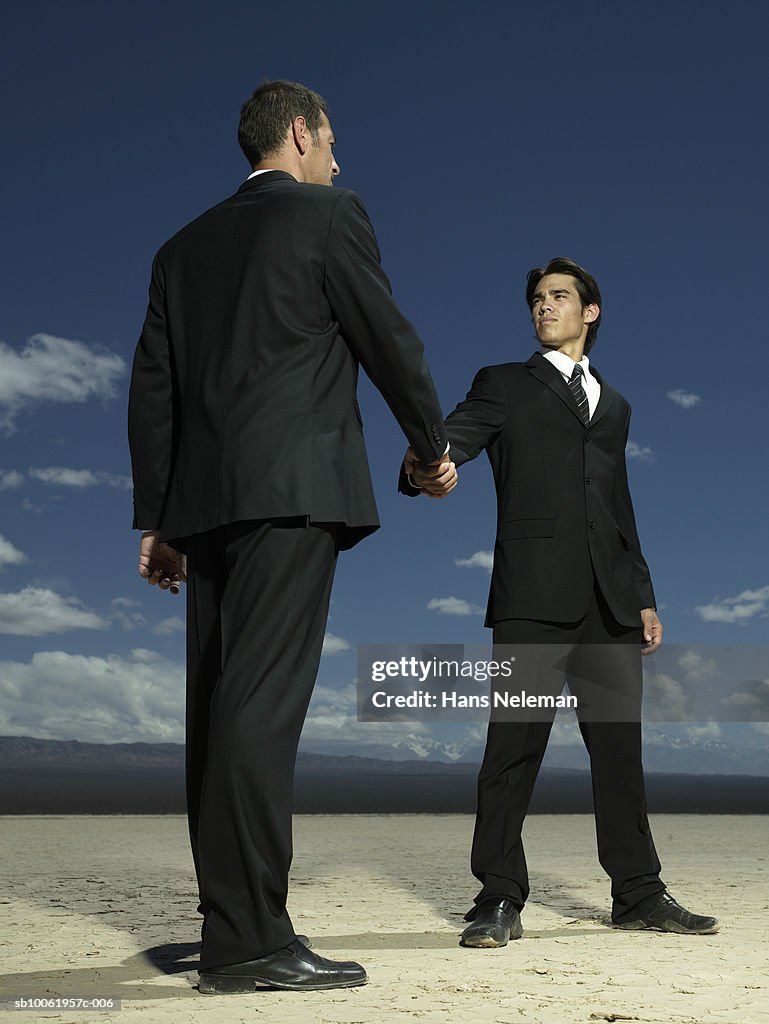 Businessmen shaking hands in desert, low angle view