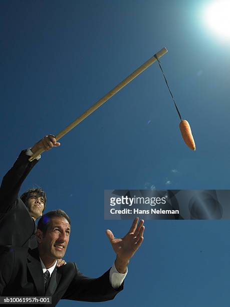 businessman dangling carrot to another businessman - dangling a carrot stock-fotos und bilder