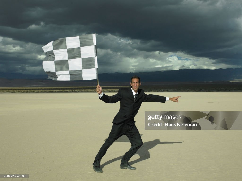 Businessman holding checkered flag in desert