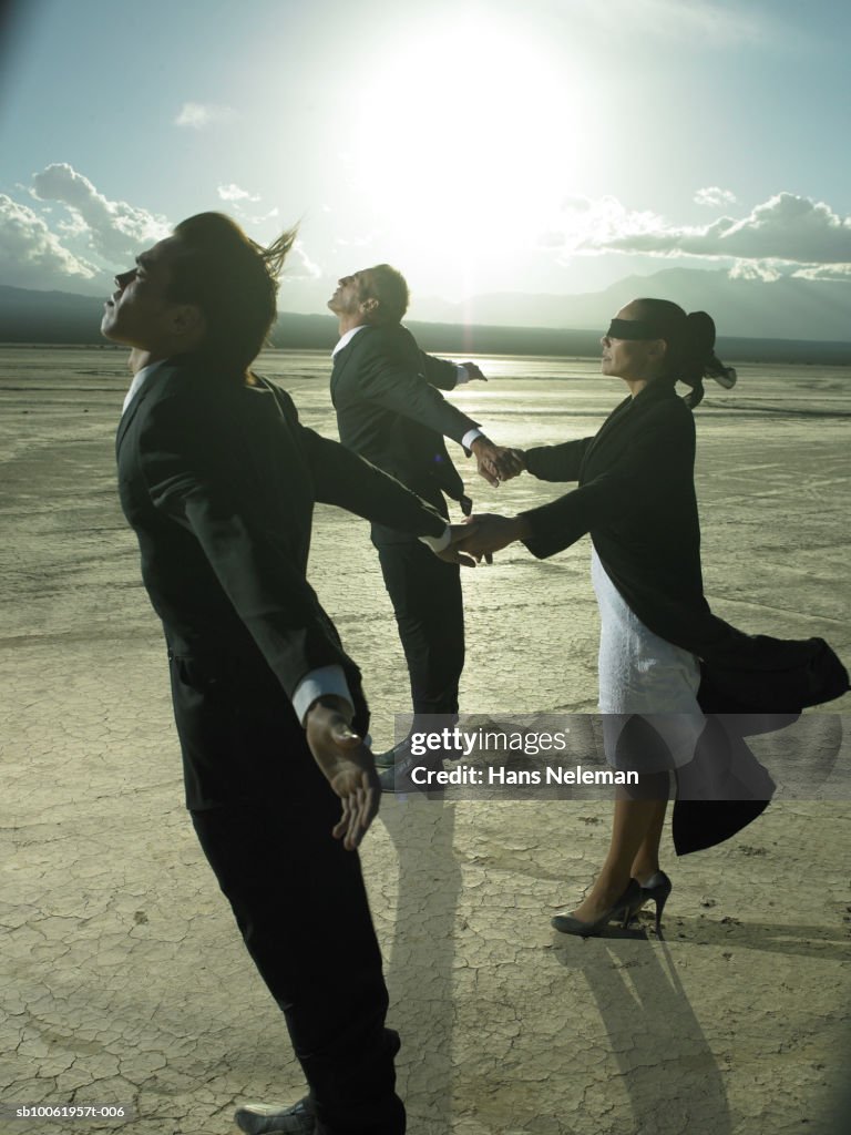 Three businesspeople holding hands in desert landscape, side view