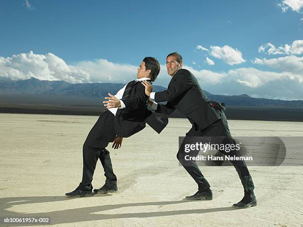 businessman pushing another businessman in desert - empurrar imagens e fotografias de stock