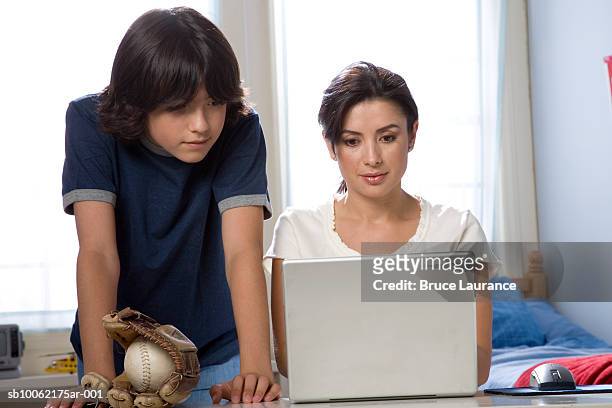 woman using laptop, son (12-13) standing by with baseball glove - baseball mom fotografías e imágenes de stock