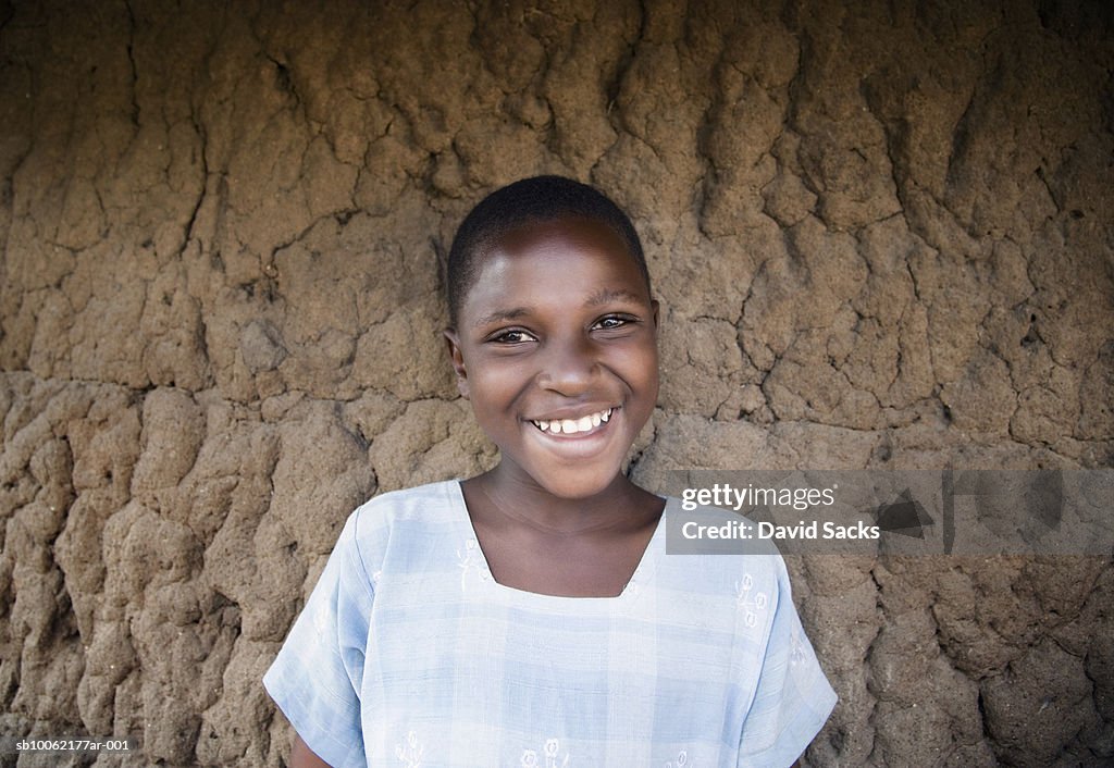 Girl (6-7) standing against wall, smiling, portrait