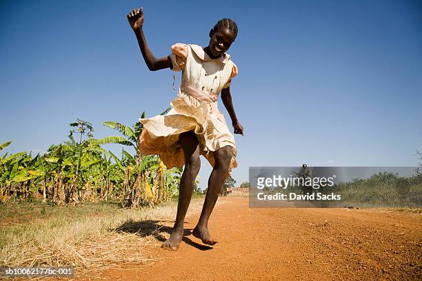 girl (8-9) running on dirt track, smiling, low angle view - third world stock-fotos und bilder