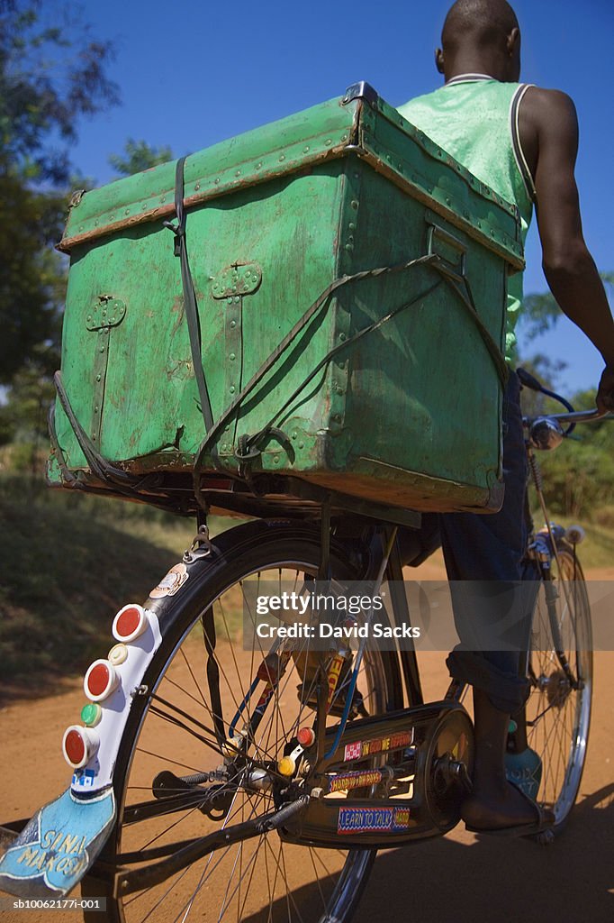 Teenage boy (16-17) carrying trunk on bicycle, low angle view