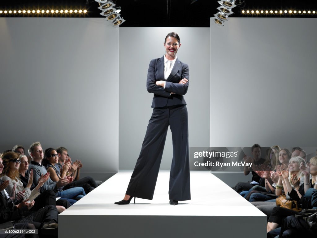 Spectators applauding female fashion designer on catwalk