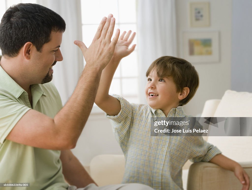 Father and son (6-7) making high five, smiling