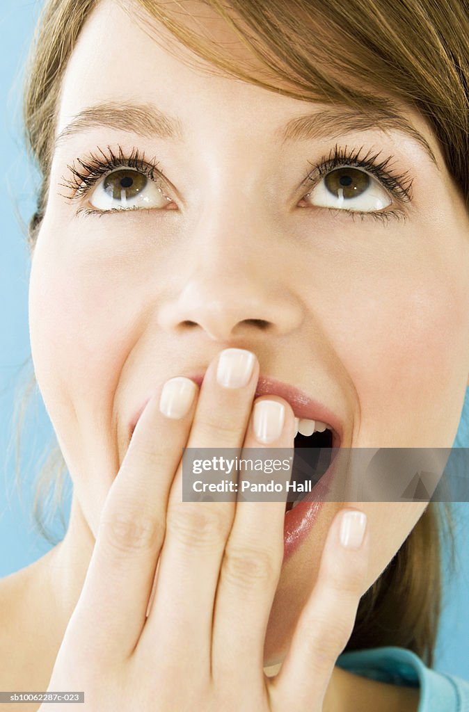 Young woman with hand over mouth, looking up, close-up