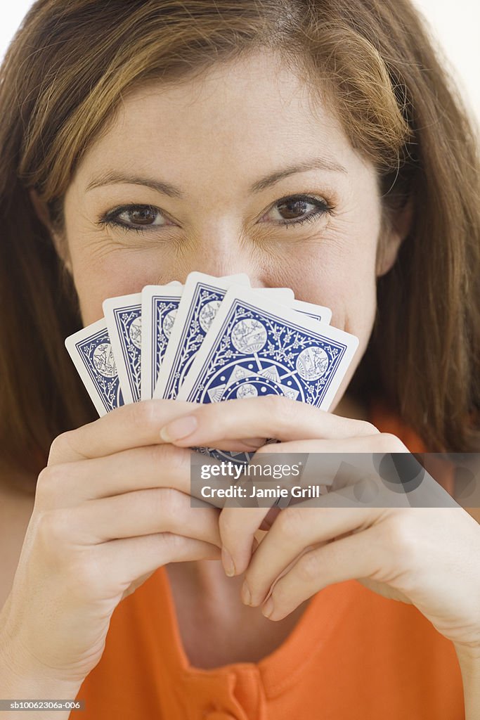 Young woman holding hand of cards, smiling, portrait