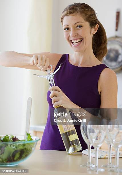young woman extracting cork from bottle of white wine, smiling, portrait - wine cork stockfoto's en -beelden