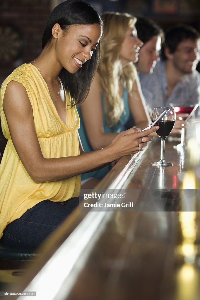 Group of friends at bar, focus on woman using mobile phone