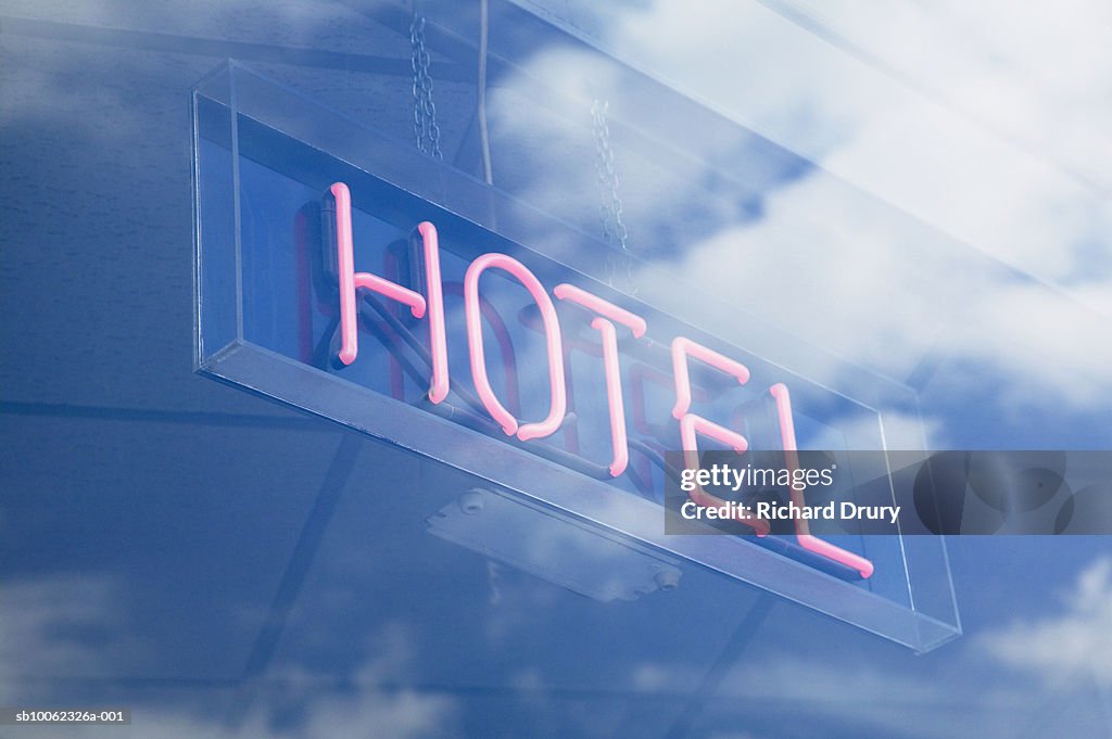 Neon Hotel sign in window reflecting sky with clouds, low angle view