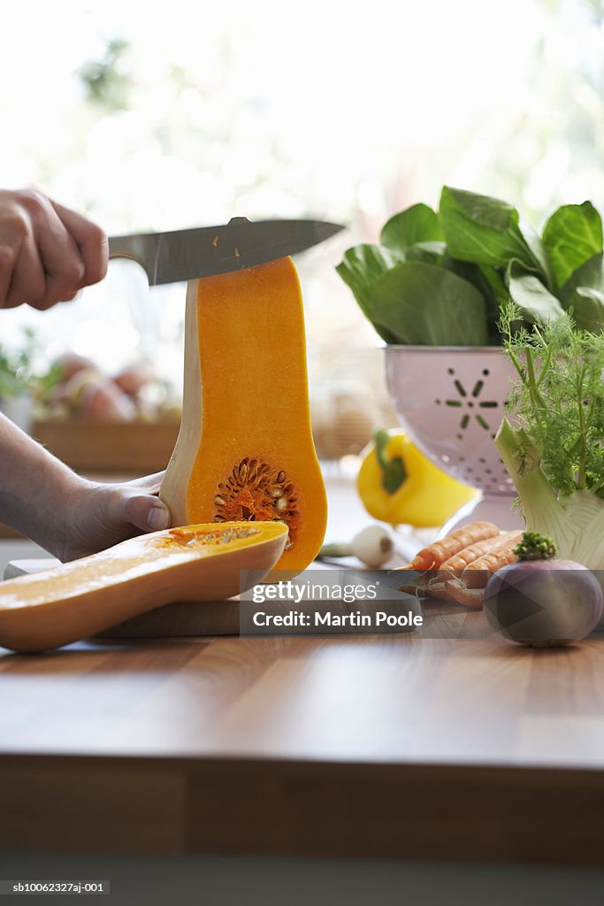 Unrecognizable person chopping pumpkin in kitchen, close-up of hands