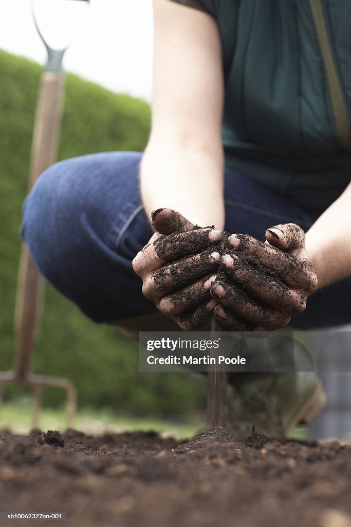 Woman crouching in field, pouring soil with cupped hands, low section