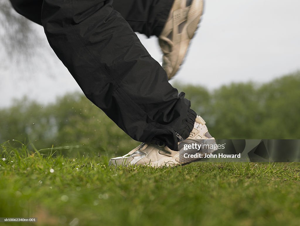 Young man running on grass, low section, blurred motion