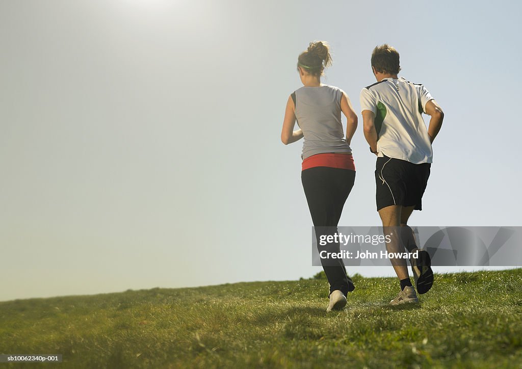 Man and woman jogging on grass, rear view
